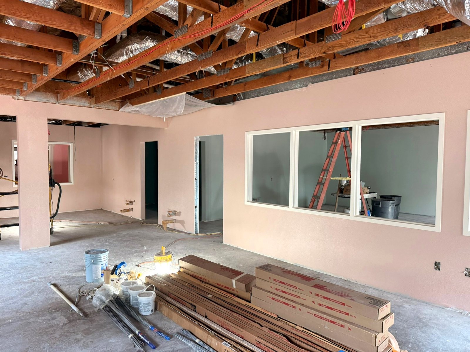 Classroom walls painted soft pink, with wide interior windows looking into the next room; ceiling framing still open above