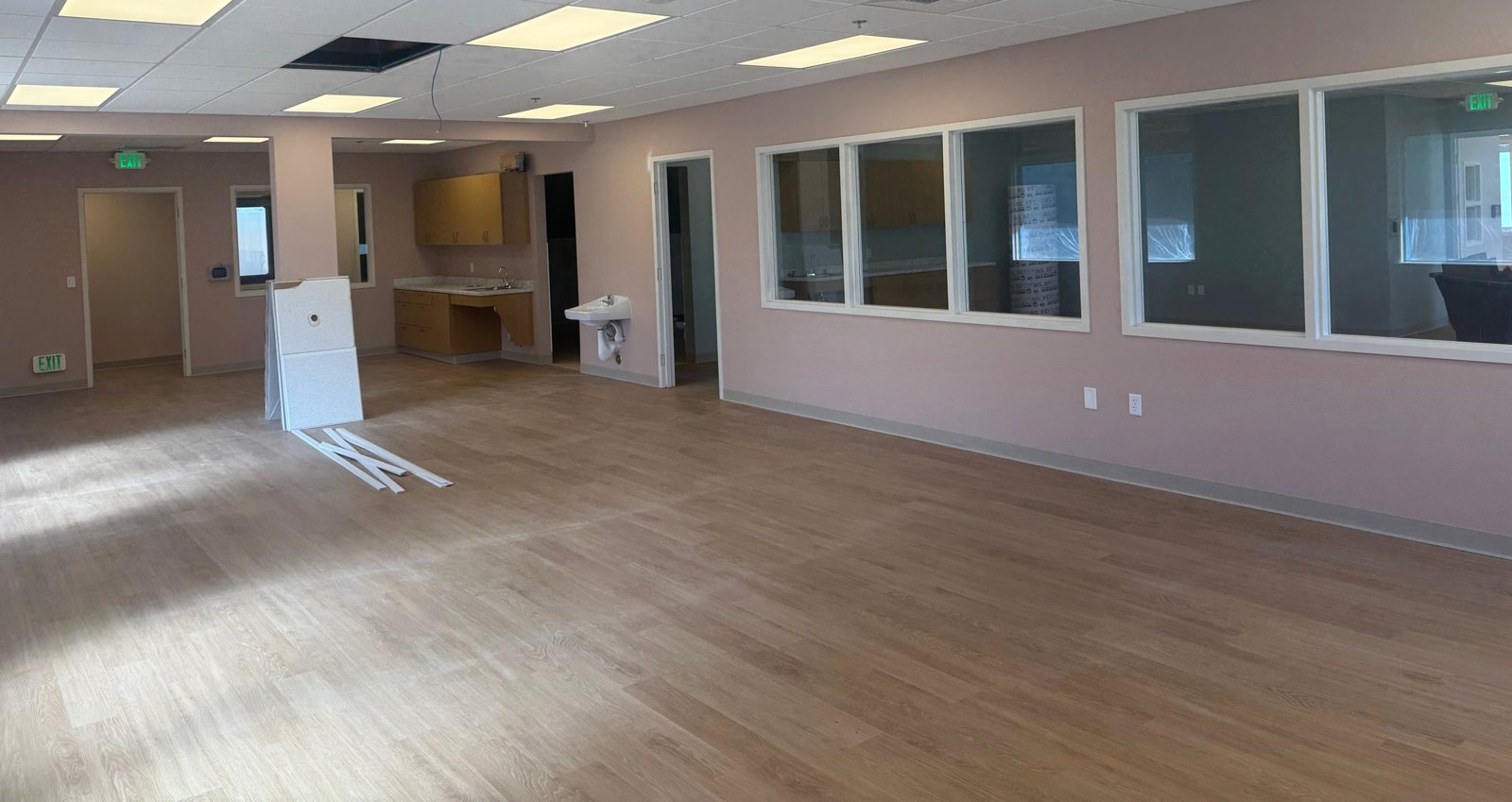 The same classroom nearly finished, with wood floors, ceiling lights, cabinets, a child-height sink, and wide interior windows